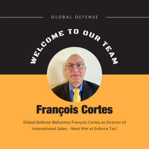 A welcome announcement graphic for Global Defense's new Director of International Sales, François Cortes. The image features a professional headshot of François Cortes, a bald man wearing glasses, a black suit, a blue shirt, and a yellow tie. The background is black and yellow, with the text "WELCOME TO OUR TEAM" in bold, curved white font above the image. Below his name, the text states: "Global Defense Welcomes François Cortes as Director of International Sales – Meet Him at Enforce Tac!